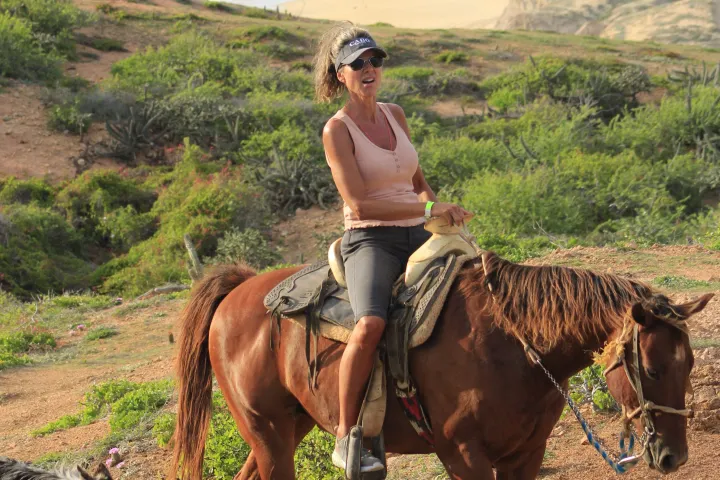 Woman on horseback with a dog by the coast.