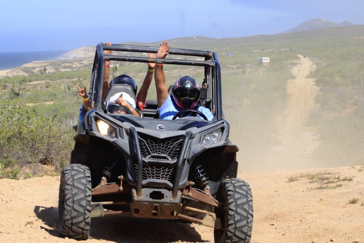 Two people riding a dune buggy on a dirt road in a desert landscape.