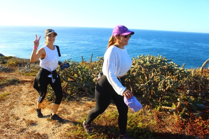 Two women hiking on a coastal trail with the ocean in the background.